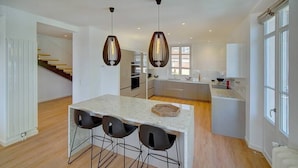 A modern kitchen with a central island, black bar stools, pendant lighting, and a view of the adjacent living area.