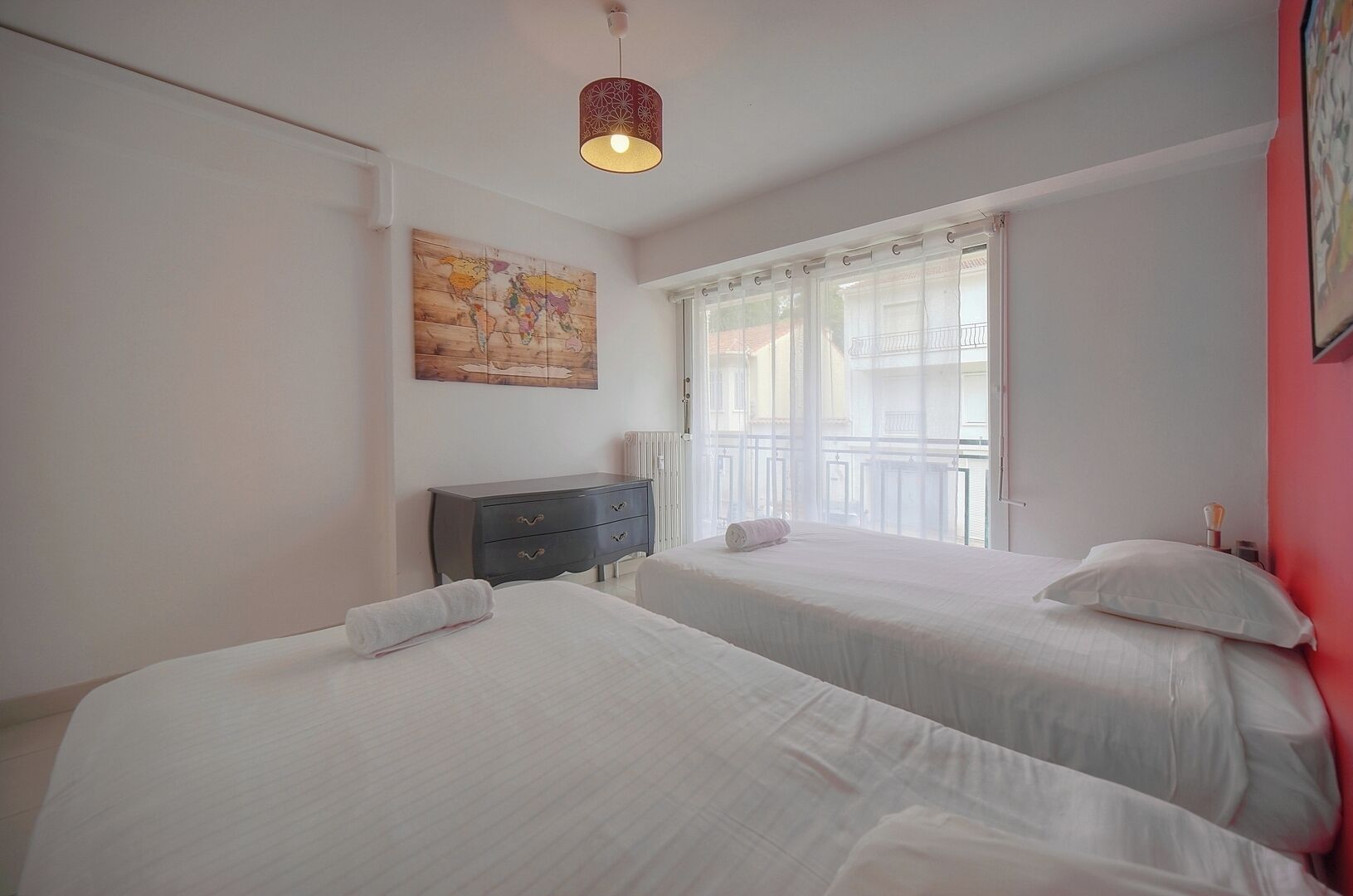A hotel room with two beds, a dresser, a world map artwork, and a window with a view of buildings.