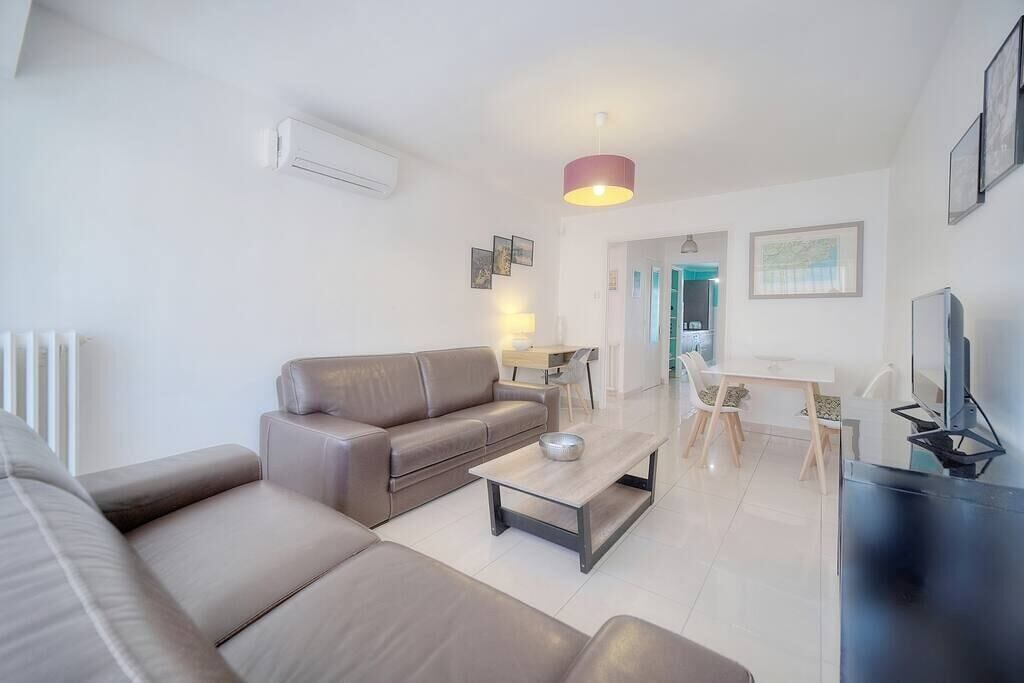 A modern living room with a sofa, a coffee table, and a television. There is a dining area with a table and chairs.