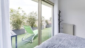 Un balcón con una silla verde, un radiador y vistas al verdor exterior.
