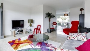 Una sala de estar moderna con un televisor de pantalla plana, sillas rojas, una mesa de centro de vidrio y una planta grande.