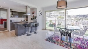 Una cocina moderna con una isla central, taburetes de bar y un comedor con una mesa de vidrio y sillas.