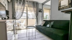 Een moderne woonkamer met een groene bank, een klein rond tafeltje en een balkon met een glazen deur.