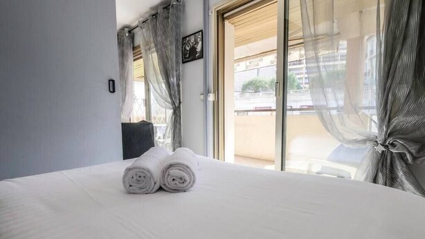 Hotelkamer met een bed, een raam met dunne gordijnen en uitzicht op het omliggende landschap.