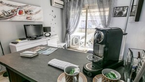 Een moderne keuken met een koffiezetapparaat, twee koffiekopjes, een laptop en een televisie op een wit kastje.
