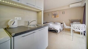 A compact hotel room with a kitchenette, a bed, a dining area, and a painting on the wall. - Upstays Terrace 25m² Studio Carnot (Cannes)