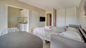 A hotel room with a bed, a desk, a chair, a TV, and a kitchenette. - Upstays Terrace 25m² Studio Carnot (Cannes)