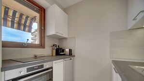 A compact kitchen with a built-in oven, a dishwasher, and a window with a striped awning. - Upstays Terrace 25m² Studio Carnot (Cannes)