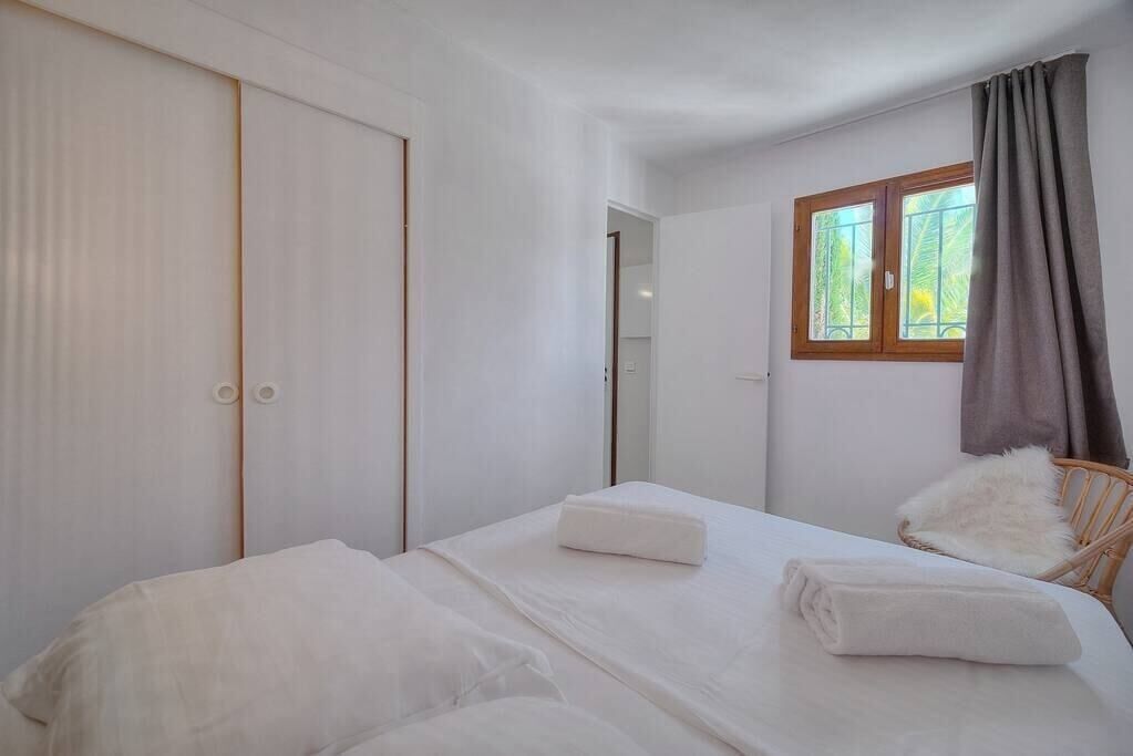 A bedroom with a bed, a wardrobe, a window with curtains, and a chair.
