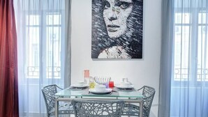 A dining area with a glass table, wicker chairs, and a large abstract painting on the wall. - Upstays Port Near 45m2 Apartment AC (Cannes)