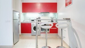 A compact kitchen with red cabinets, a washing machine, and two white bar stools. - Upstays Port Near 45m2 Apartment AC (Cannes)