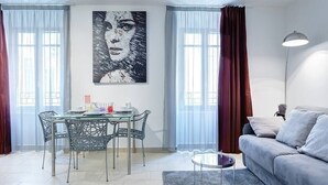 A modern living room with a glass dining table, metal chairs, a grey sofa, and a large abstract painting on the wall. - Upstays Port Near 45m2 Apartment AC (Cannes)