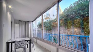 Un balcon donnant sur un jardin et des immeubles, une table à manger avec des chaises et une rambarde bleue.