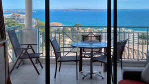 A balcony with a table and chairs, overlooking a coastal view.