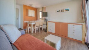 A compact living space with a sofa, a dining table with chairs, a small kitchenette, and a TV.