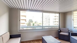 A balcony with wicker furniture, a view of buildings, and a wooden floor. - Upstays Croisette Veranda 48m² Apartment (Cannes)