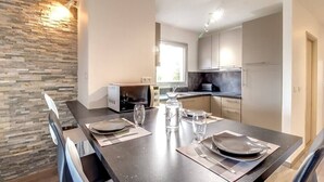 A modern kitchen with a stone wall, a dining table set for four, and a microwave. - Upstays Croisette Veranda 48m² Apartment (Cannes)
