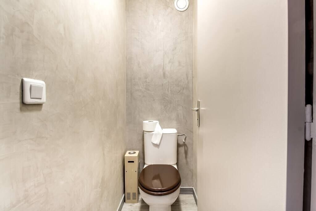 Un baño con inodoro, dispensador de toallas de papel e interruptor de luz en la pared.
