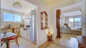 A spacious kitchen with white cabinets, a dining table with red chairs, and a large window. - Upstays Sea View Terrace 60m² Apartment (Cannes)