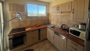 A compact kitchen with a window, a stove, a sink, a microwave, and wooden cabinets. - Upstays Sea View Terrace 60m² Apartment (Cannes)