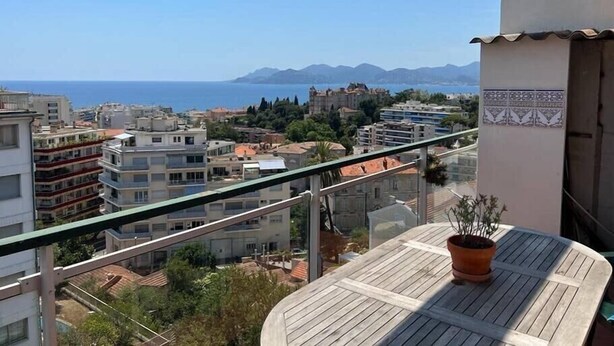 A balcony with a view of the sea and mountains, a potted plant, and a tiled table. - Upstays Sea View Terrace 60m² Apartment (Cannes)