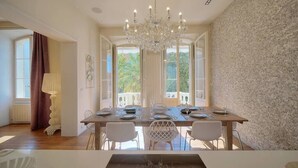 A dining room with a chandelier, white chairs, and a large window with a view of greenery.