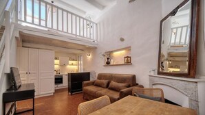 Amplia sala de estar con una mesa de comedor, un sofá y una chimenea. Se ve una cocina al fondo y un balcón en lo alto.