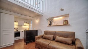 Una sala de estar acogedora con un sofá de cuero marrón, una cocina al fondo y una escalera blanca que sube a un nivel superior.