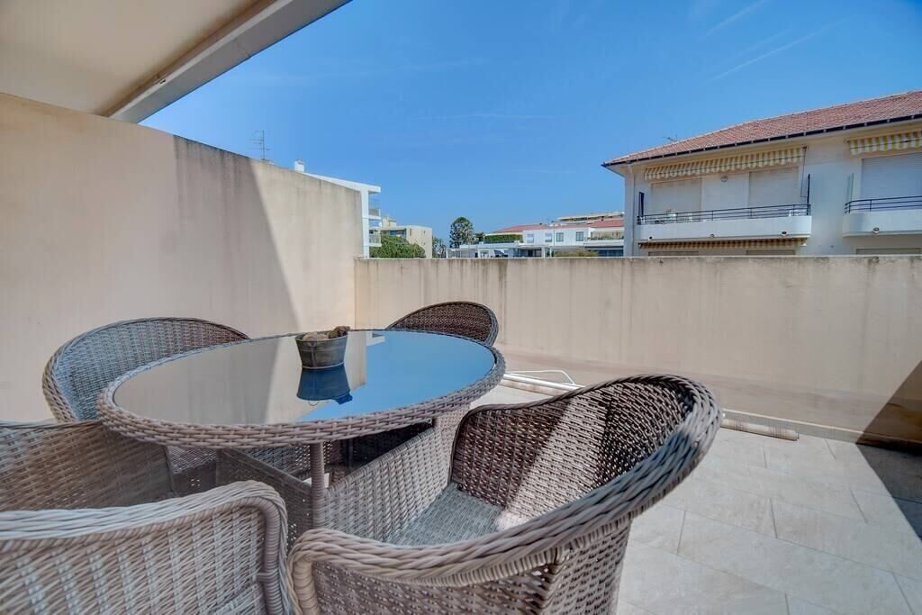 A balcony with wicker furniture, a glass table, and a view of buildings in the background.