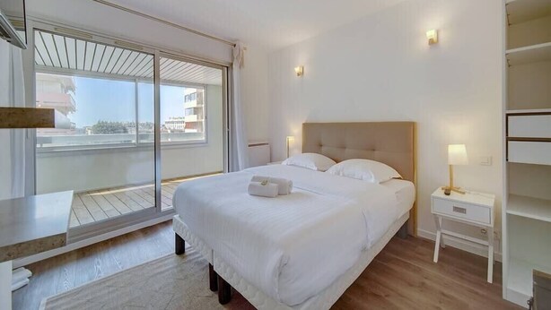 Een hotelkamer met een groot bed, een nachtkastje met een lamp, een raam met uitzicht op gebouwen en een klein bureau.