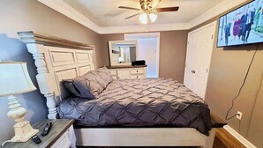 A bedroom with a bed, a nightstand, a dresser, a ceiling fan, a mirror, and a television.