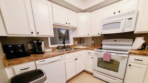 A kitchen with white cabinets, a microwave, a stove, a coffee maker, and a trash bin.