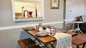 A dining area with a table set for four, a mirror above, and a framed picture on the wall.