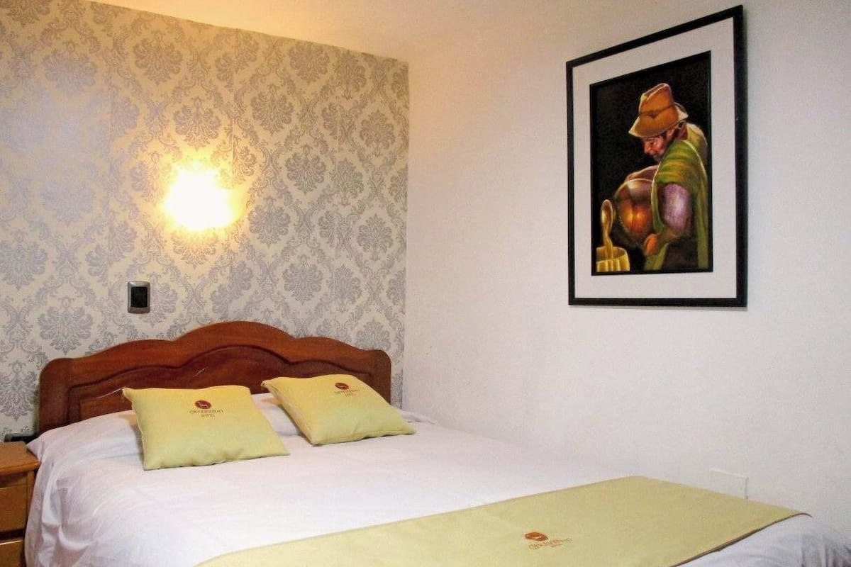 Ein Hotelzimmer mit Bett, zwei Kissen, einem Nachttisch, einem gerahmten Bild an der Wand und einer Wandleuchte.