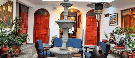 A courtyard with a central fountain, red doors, and potted plants.