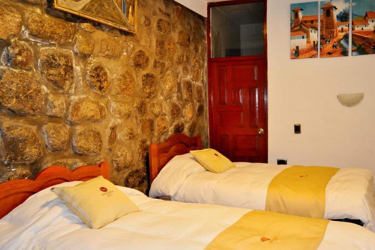 Ein Zimmer mit zwei Betten, einer Steinwand, einer roter Tür und einem Gemälde an der Wand.