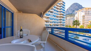 Un balcon avec une table dressée pour le dîner, une bouteille de vin et un verre. Le balcon offre une vue sur une piscine et un paysage montagneux.