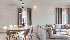 A modern living room with a grey sofa, a dining table with chairs, and a hanging light fixture. - Vacation home Romeo by Interhome (Pula/Vodnjan)