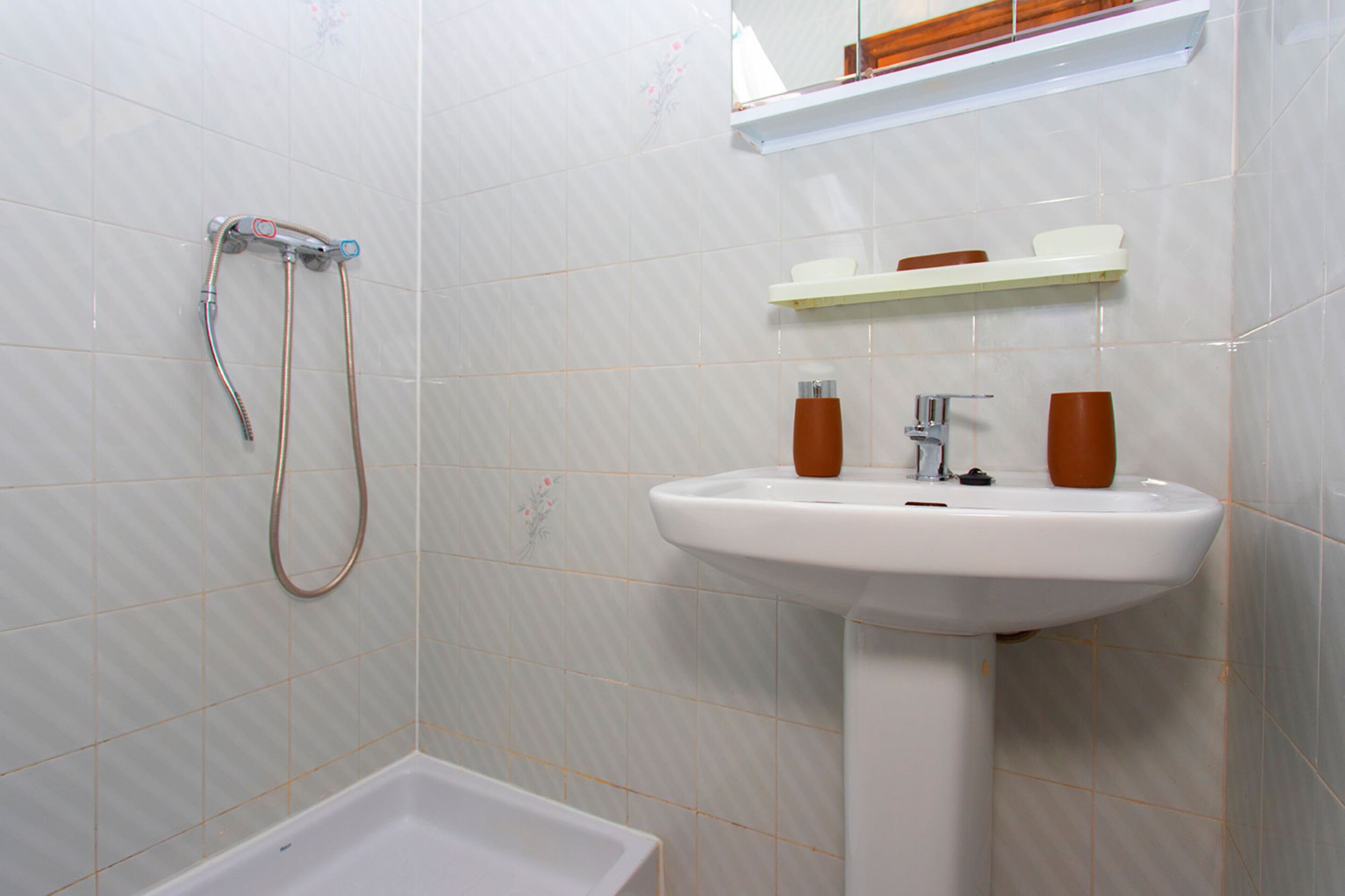 Une salle de bain avec un lavabo blanc, une douche et un miroir au-dessus du lavabo.