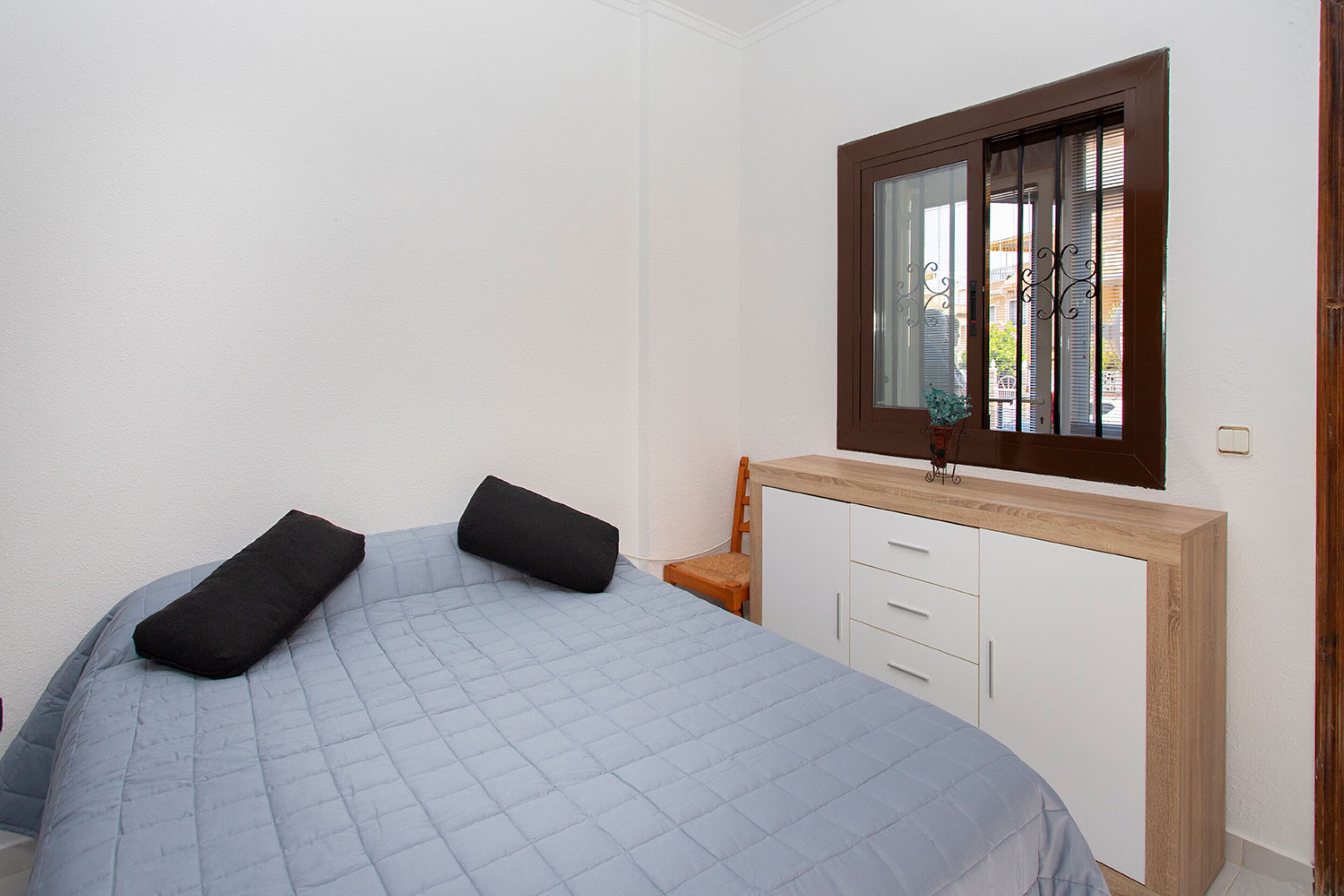 Een slaapkamer met een bed, een houten nachtkastje, een raam en een witte kledingkast.