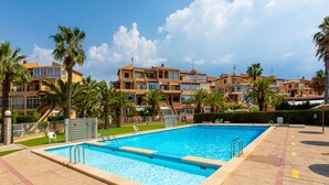 Una piscina con bordo piastrellato, circondata da palme e da una fila di edifici a più piani.