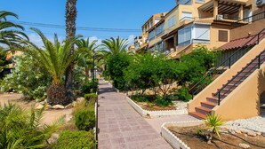 Zona residenziale con vialetto lastricato, palme e una scala che conduce a un edificio con balconi.