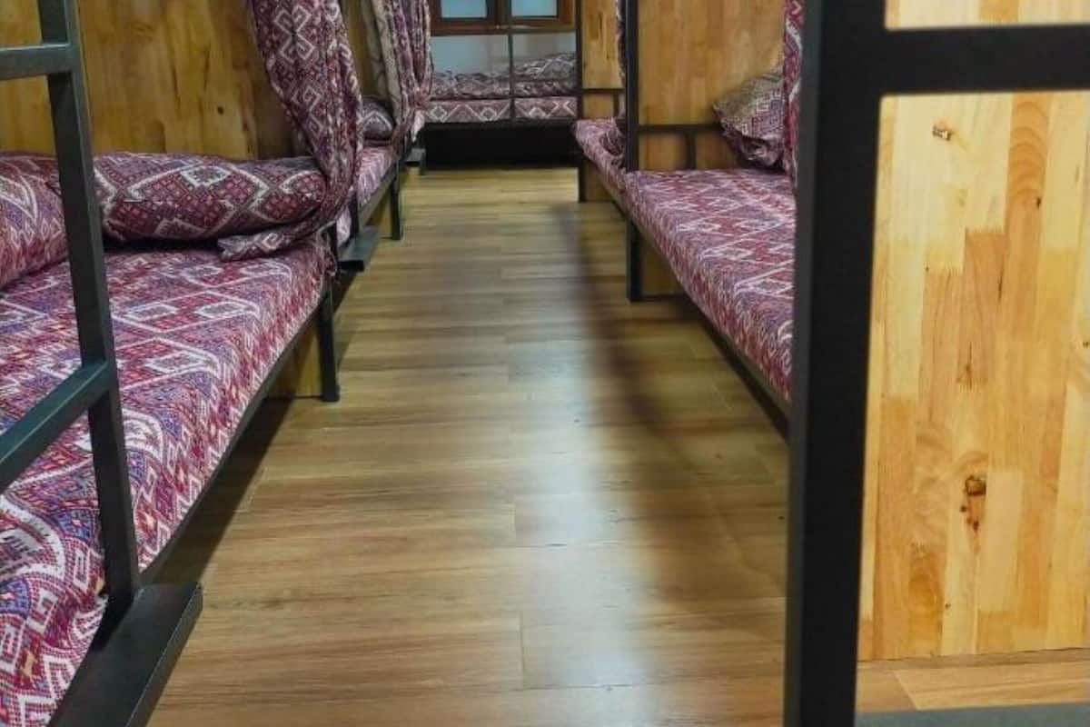 A bunk bed room with wooden walls and floors, patterned bedding, and a window at the end of the room.