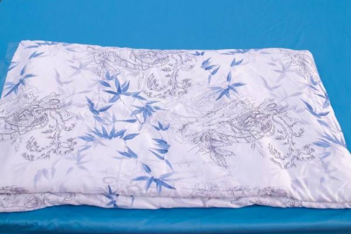 A bed with a blue mattress and white bedding with a leaf pattern.