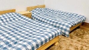 A room with two single beds, wooden headboards, a white wall, and a ceiling light. - Doi Thong Homestay (Ha Giang 1)