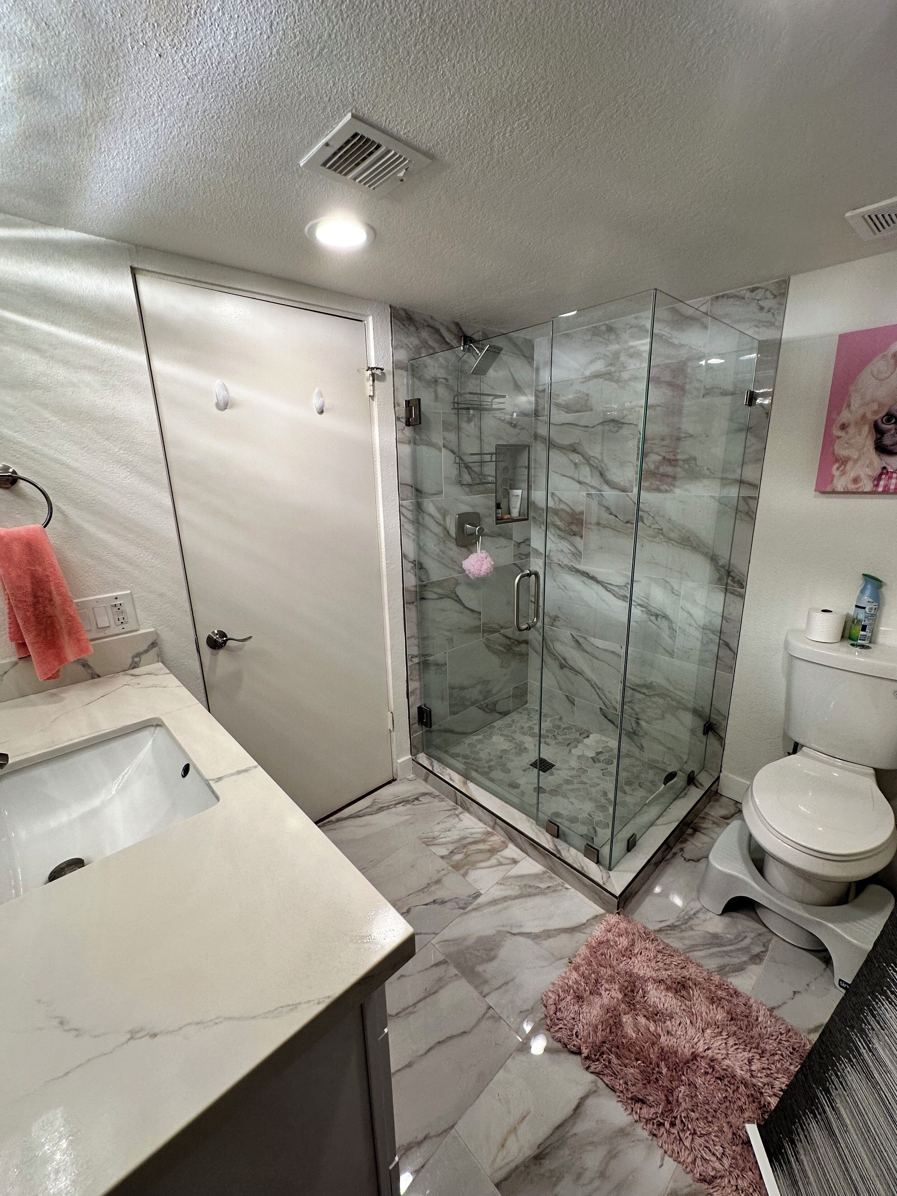Ein Badezimmer mit einer gläsernen Duschkabine, einem мраморным Waschbecken und einer Toilette.
