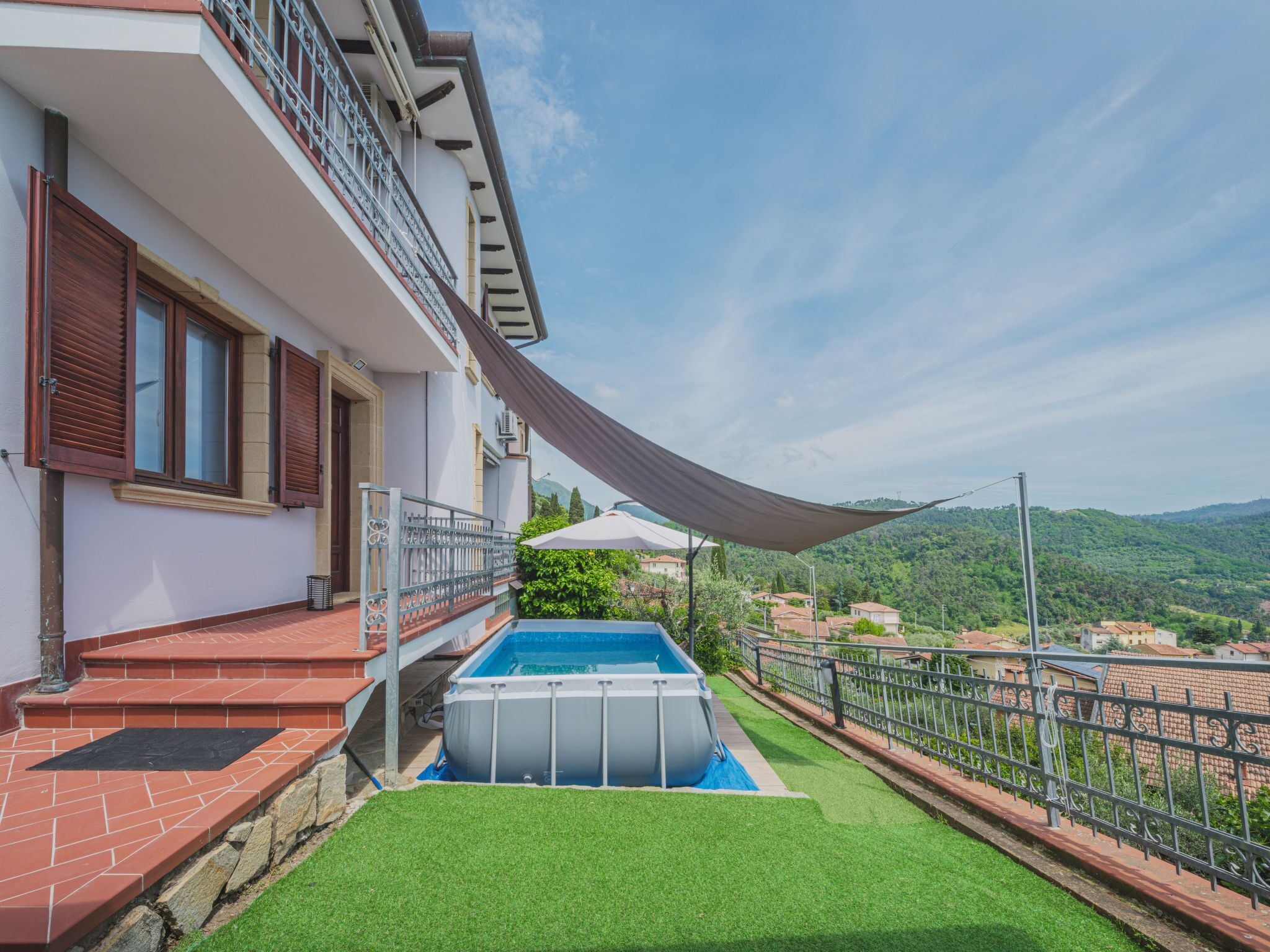 Ein Wohnhaus mit Swimmingpool, einem Balkon mit Metallgeländer und Blick auf eine hügelige Landschaft.