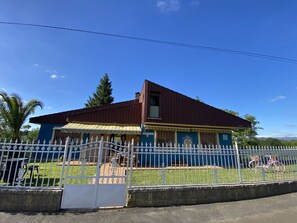 Un bâtiment à deux étages, avec un toit rouge et une façade bleue, entouré d’une clôture blanche.
