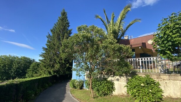 A curved road with a building on the right, surrounded by greenery and trees. - Vivienda Vacacional La Casa Azul ll (Ceceda)
