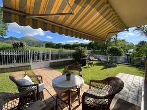 Une terrasse extérieure avec des meubles en osier, un espace abrité et une vue sur un paysage montagneux.